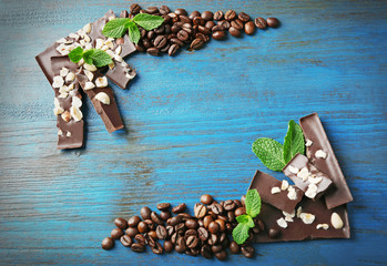 Black chocolate pieces with nuts  and coffee grains on color wooden background
