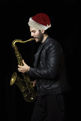 Naklejka na ściany i meble A saxophone player in Santa Claus hat a dark background. Christm