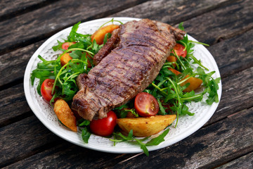 rare beef steak with roasted potatoes, tomatoes and wild rocket leaves. on old wooden table