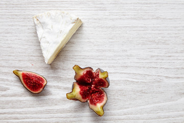 Piece of camember with splittef fig on white wooden table