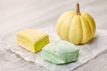Side view of two pastel marshmallows and small pumpkin on white