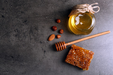 Honeycomb, glass pot with honey and nuts on gray background