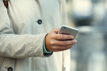 A female hand holding a mobile phone outdoors, on blurred background