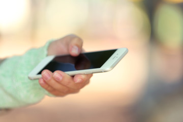 A female hand holding a mobile phone outdoors, on blurred background