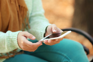 Female hands holding a mobile phone outdoors, on blurred background