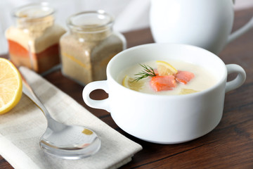 Delicious salmon cream soup on wooden table, which served with sliced lemon and spices