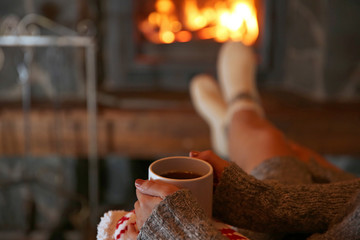 Woman resting with cup of hot drink near fireplace
