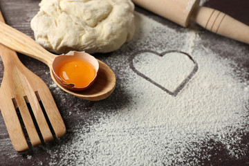 Heart of flour, croissant and  wooden kitchen utensils on gray background