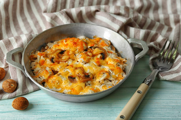 Roasted mushrooms, chicken and cheese gratin in pan, on wooden background