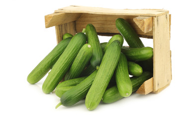 fresh green snack cucumbers in a wooden box on a white background