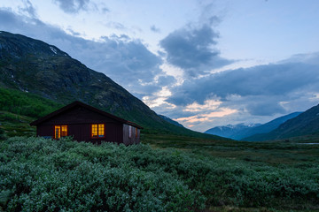Life in the mountains. Wooden house with light on the evening mountains. Fairytale in Norway
