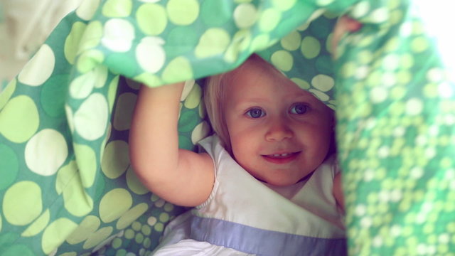Cheerful baby girl playing hide and seek, cute playful child hiding under the covers, having fun at home, happy carefree childhood. Full HD Video 1920x1080
