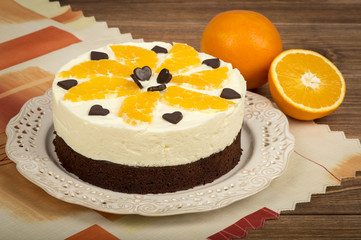 Brownie cake with cream and oranges on the wooden background.