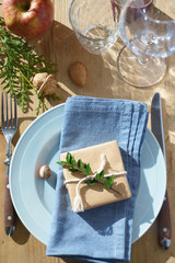 Rustic table setting: small present wrapped with kraft paper, evergreens, nuts, apple