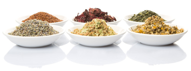 Dried herbal tea leaves, lavender, rooibos, chamomile, linden flower, hibiscus, Japanese green tea in white bowl over white background