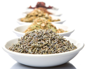 Dried herbal tea leaves, lavender, rooibos, chamomile, linden flower, hibiscus, Japanese green tea in white bowl over white background