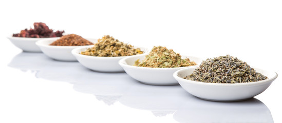Dried herbal tea leaves, lavender, rooibos, chamomile, linden flower, hibiscus, Japanese green tea in white bowl over white background