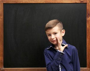 Cute boy posing at the clean blackboard, in the classroom