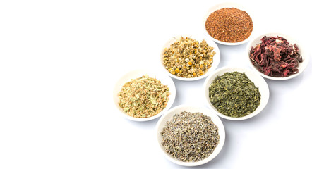 Dried herbal tea leaves, lavender, rooibos, chamomile, linden flower, hibiscus, Japanese green tea in white bowl over white background