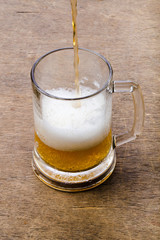 Beer being poured into beer glass creating foam and bubbles on wood texture
