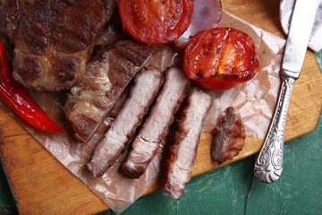 Roasted beef fillet and vegetables on cutting board, on wooden background