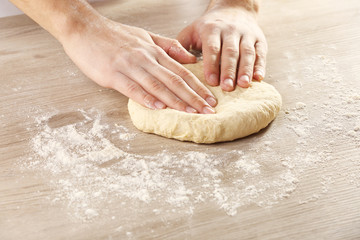 Hands kneading dough for pizza on the wooden table, close-up