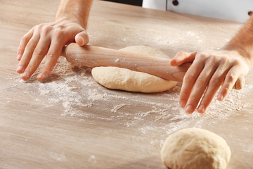 Hands rolling dough for pizza on the wooden table, close-up
