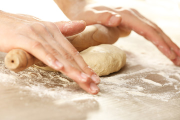 Hands rolling dough for pizza on the wooden table, close-up
