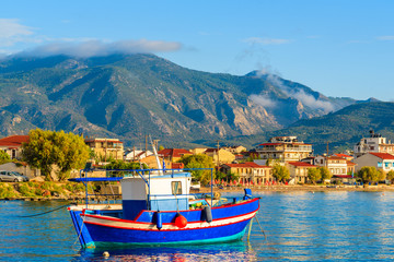 Greek fishing boat on sea with colourful houses in background at sunrise time on Samos island,...