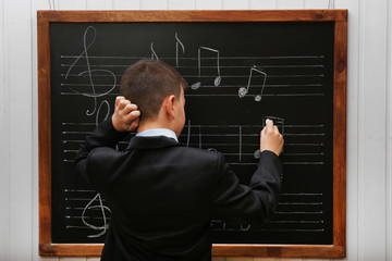 Young cute schoolboy standing at the blackboard with musical notes