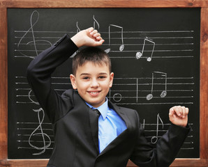 Young cute schoolboy posing at the blackboard with musical notes