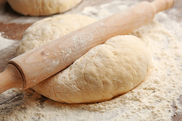 Dough for pizza and rolling-pin on wooden table