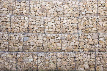 Rocky stony wall texture with metallic net to keep together every small rock in a train station.