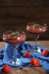 Chocolate dessert in glasses and fresh berries on color wooden background