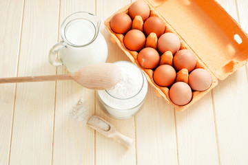 
the ingredients for the dough , eggs , milk, butter , salt and flour on a wooden background