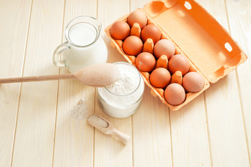 
the ingredients for the dough , eggs , milk, butter , salt and flour on a wooden background
