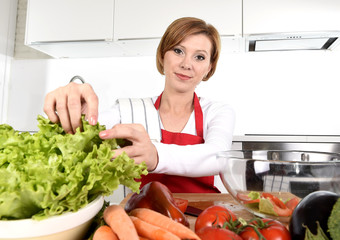 young beautiful woman in red apron at home kitchen preparing vegetable salad bowl smiling happy