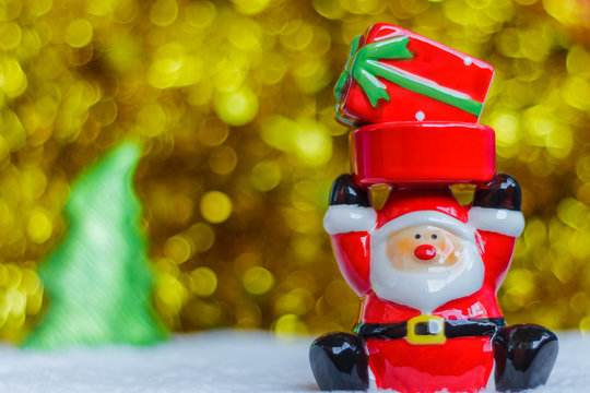 Santa Claus carrying a red gift box and blurred golden sparking bokeh and christmas tree background (selective focus on face of Santa)