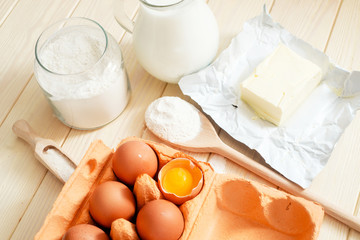 
the ingredients for the dough , eggs , milk, butter , salt and flour on a wooden background