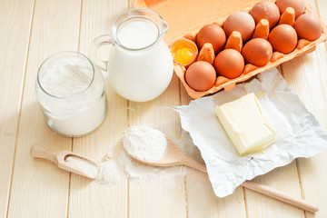 
the ingredients for the dough , eggs , milk, butter , salt and flour on a wooden background