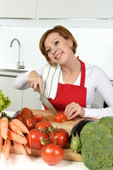 happy woman at home kitchen preparing vegetable salad with lettuce, carrots and slicing tomato smiling