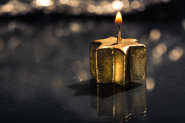 Goldene Kerze mit Reflektion auf schwarzem Untergrund, unscharfe