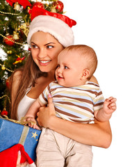 Mom wearing Santa hat holding  baby  under Christmas tree.