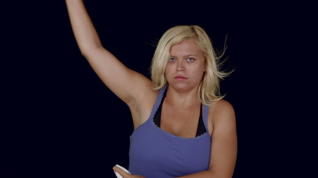 Young blond woman using deodorant spray on underarm, studio isolated.