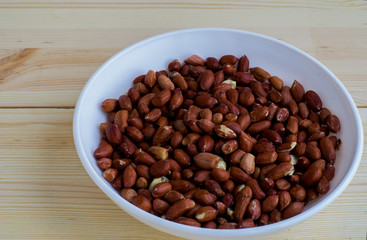Raw peanuts in a white bowl on wood background