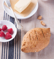 Homemade oatmeal bread on a wooden table with coffee, butter and raspberries for breakfast. Square format.