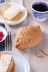 Homemade oatmeal bread on a wooden table with coffee, butter and raspberries for breakfast..