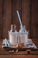 Homemade walnut nut milk in glass bottles with blue straw on a wooden background..