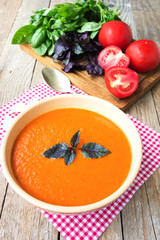 Fresh tomato soup with basil and tomatoes on wooden table