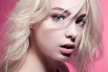 Close-up portrait of a woman with beautiful eyes and blonde hair on a pink background